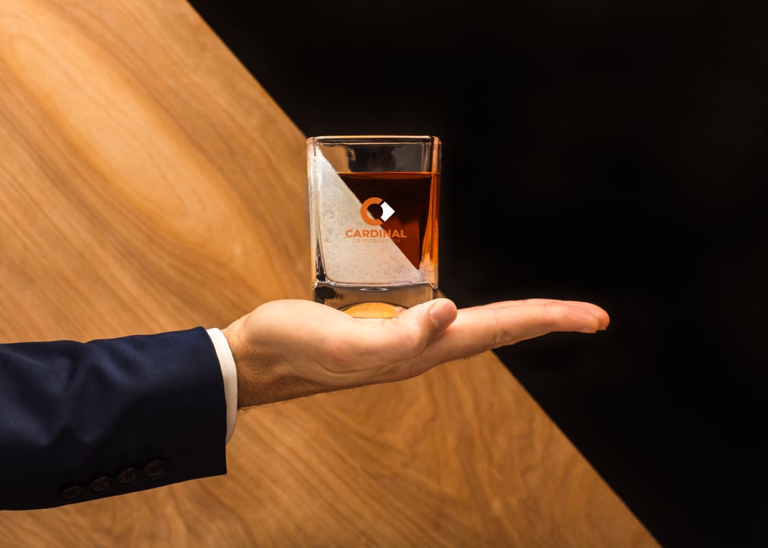 A person holds a branded whisky glass that contains an ice wedge.